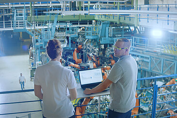 Zwei Personen mit einem Laptop in einer Fabrik.