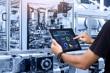 Mitarbeiter mit Tablet in der Hand prüft Performance einer Maschine.